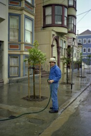 Man standing on the sidewalk holding a hose in the rain