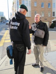 Man being interviewed on a street corner by another man with recording equipment
